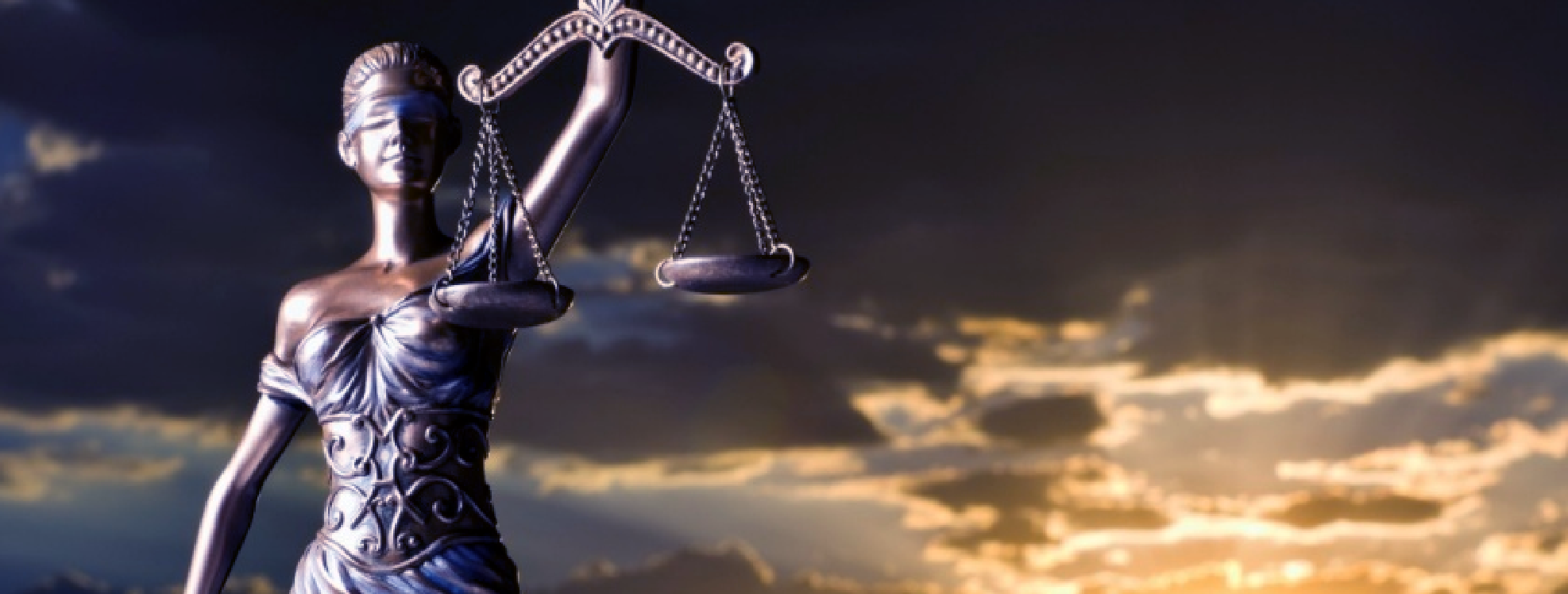 Lady Justice statue holding scales against a cloudy sky